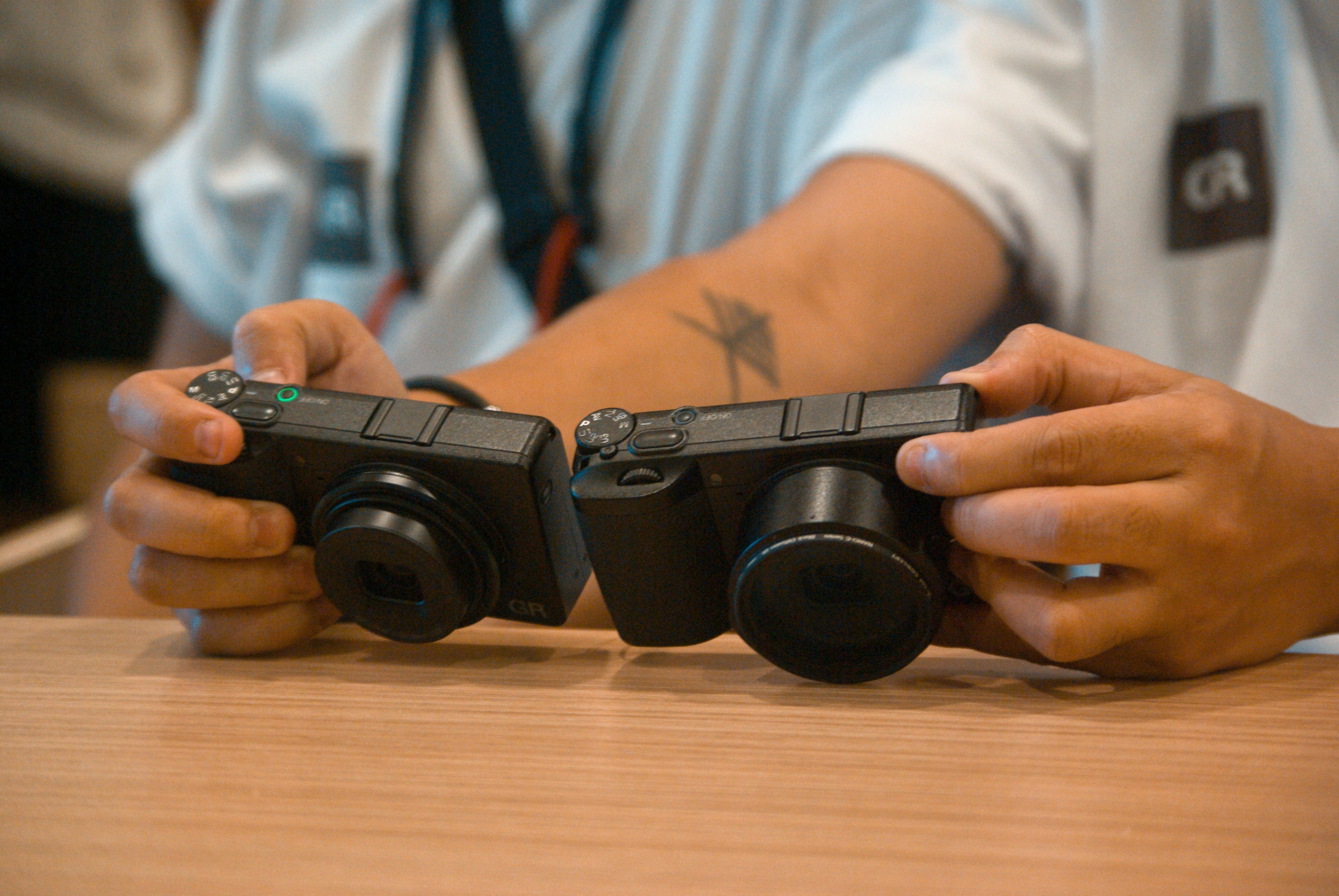 Hands testing and reviewing two compact cameras on a wooden table